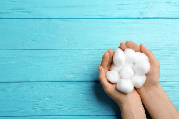 Woman holding cotton balls on color wooden background, top view. Space for text - 写真・画像