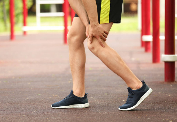 Νεαρός άνδρας που υποφέρει από πόνο στο γόνατο σε αθλητικό έδαφος, κοντινό πλάνο - Φωτογραφία, εικόνα