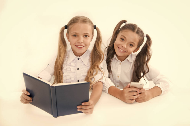 Getting information. Modern data storage instead big paper book. Little girls read paper book and ebook smartphone. Application for education. Educational application mobile phone. Education online - Фото, изображение