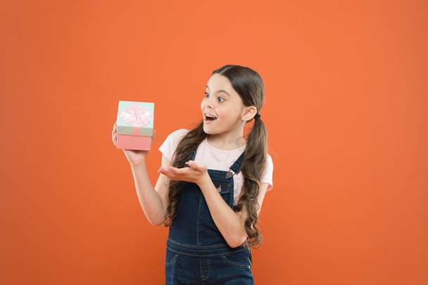 The best present ever. Small child holding birthday present on orange background. Little girl with wrapped present box. Surprised kid receiving present on boxing day - Zdjęcie, obraz