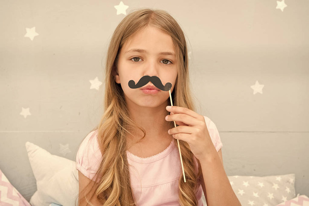 Pajamas party concept. Girl fake mustache at pajamas party. Cheerful kid posing mustache. Photo booth props ideas. Printable accessories for party. Girl long blonde hair posing with photo booth props - Foto, Imagem