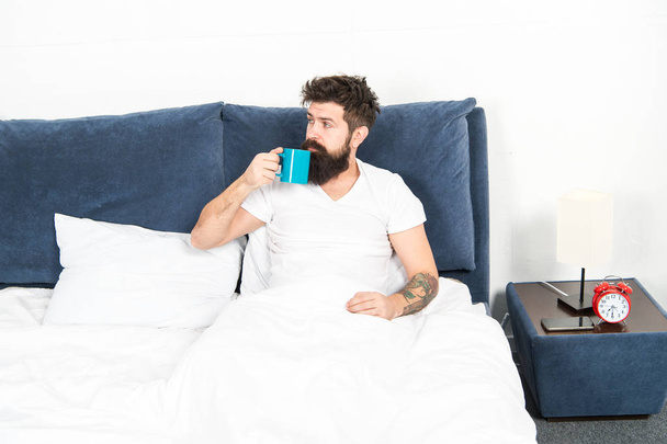Humanity runs on coffee. Man brutal handsome hipster relaxing bedroom drink coffee. Bearded guy enjoy morning coffee. Tune in to new day. Morning awakening better with cup coffee. Relax and rest - Foto, Imagem