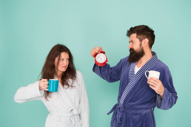 Time to wake up and have nice day. Guy husband hold coffee and clock. Every morning begins with coffee. Couple in bathrobes with mugs. Man with beard and sleepy woman enjoy morning coffee or tea - Φωτογραφία, εικόνα
