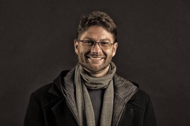 Fashion model with beard smile on dark background. Happy man in glasses on bearded face. Bearded man in scarf and coat on dark background. Autumn style and trend. Fashion accessory, vintage filter - Foto, afbeelding