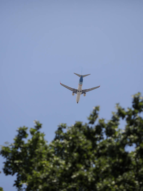 Commercial airline airplane can be seen flying above green trees - Photo, Image