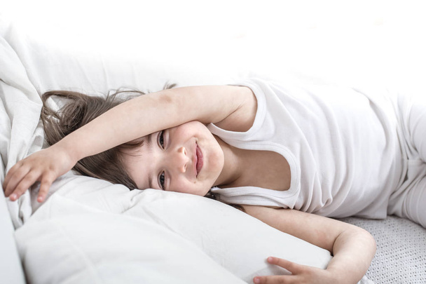 Petite fille mignonne souriant tout en étant allongé dans un lit blanc confortable
 - Photo, image