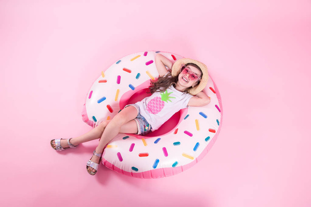 A little child girl lying on a donut inflatable circle. Pink bac - Zdjęcie, obraz