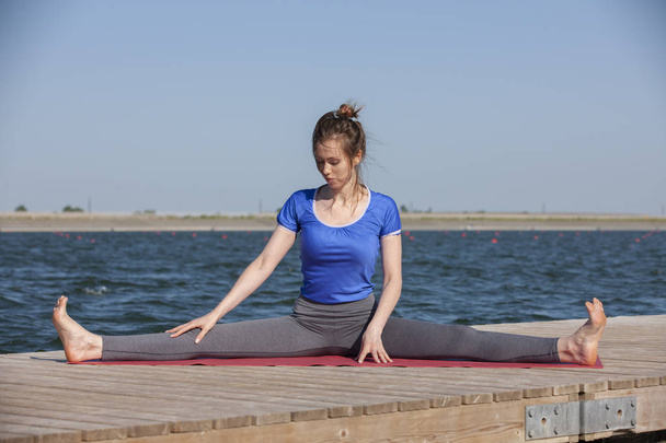 Girl practicing yoga near lake, enjoying nice day in nature and positive energy. - Zdjęcie, obraz