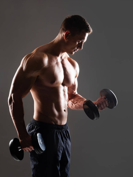 Strong, fit and sporty bodybuilder man with dumbbells over black background. Sport and fitness concept. - Фото, изображение