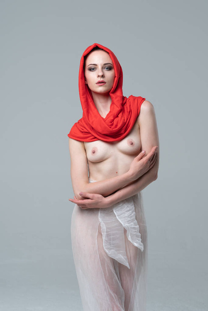 young beautiful girl posing nude in the studio, standing in a red scarf and white pants - 写真・画像