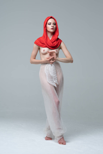 young beautiful girl posing nude in transparent white clothes and red scarf, stands near the white wall - Foto, Imagen