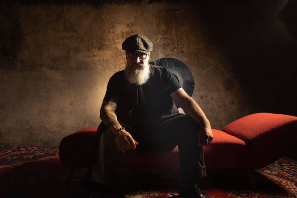 Kollarında dövmeli sakallı hipster portresi kanepede otururken - Fotoğraf, Görsel