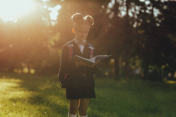 schoolgirl reads a book in the park, in school uniform, outdoor, at sunset - Photo, Image