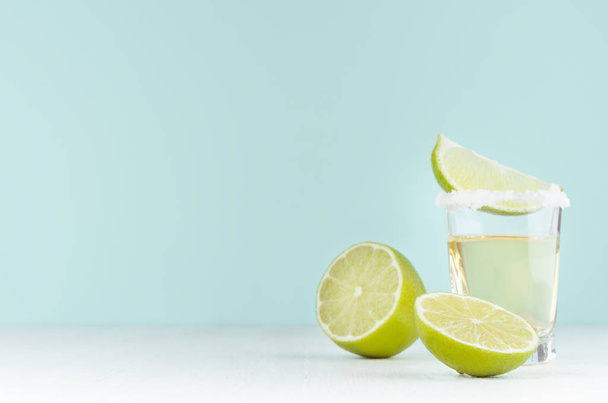 Cooking of summer fresh alcohol shot of tequila with lime, salt on rim on soft light pastel green background and white wood table. - Fotoğraf, Görsel