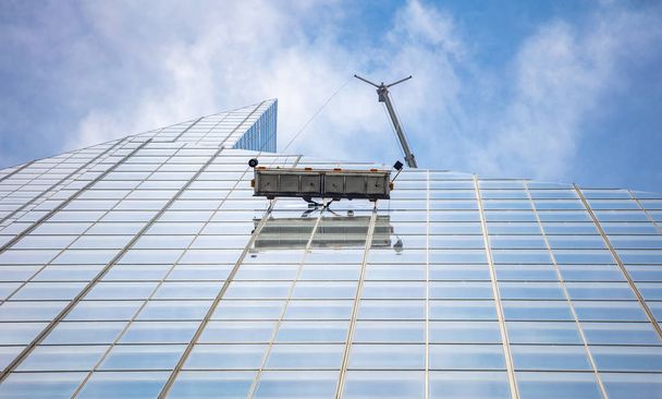 New York, Manhattan. Glas reinigingsdiensten, hoge gebouw glazen gevel, uitzicht van onder tegen blauwe hemel achtergrond - Foto, afbeelding