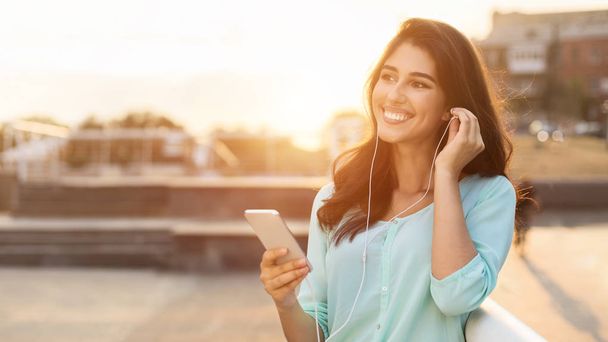 Woman enjoying music in earphones, having walk in the city - Zdjęcie, obraz