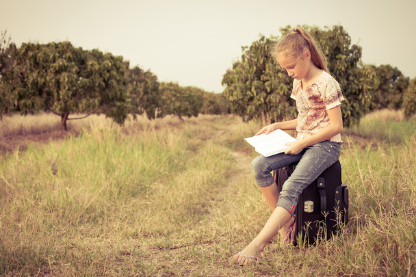 Little girl sitting and reading a book on nature - Foto, imagen