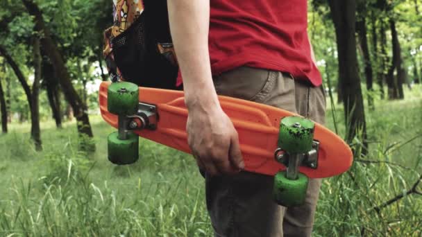 Hipster skateboarder soggiorno sul parco tenendo lo skateboard in mano, giornata di sole all'aperto
. - Filmati, video