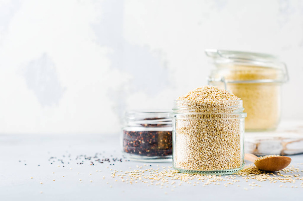Raw quinoa grains in jar. Healthy vegetarian food on gray kitchen table. Selective focus. - Valokuva, kuva