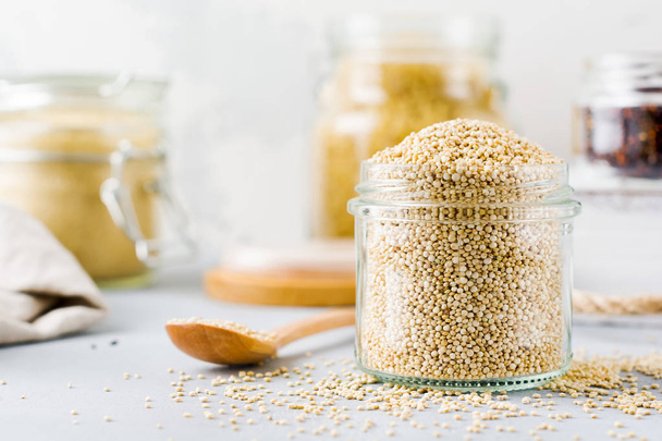 Raw quinoa grains in jar. Healthy vegetarian food on gray kitchen table. Selective focus. - Photo, Image