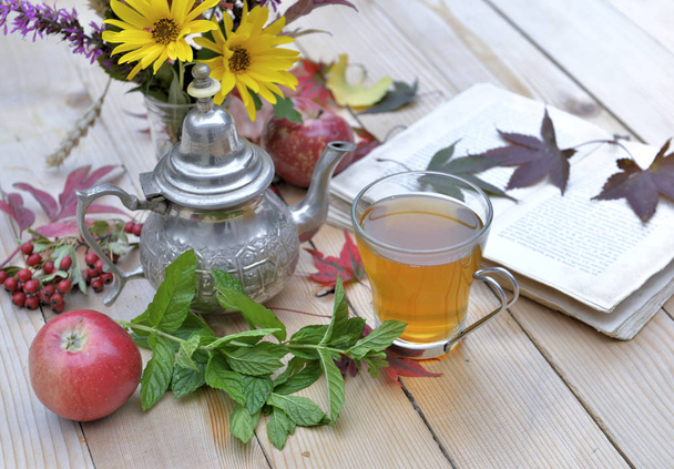 šálek mátového čaje na zahradní stolek s květinami a s knihou pro relaxační okamžik na podzim  - Fotografie, Obrázek