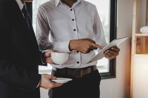 two partner business man investor holding coffee cup up and talking and reading information about financial statistics in mobile tablet standing in office, encouragement and digital technology concept - Foto, immagini