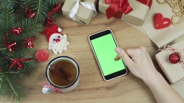 Joulun idea. Huippunäkymä. Musta puhelin vaaleanpunainen tapauksessa vihreä näyttö kevyt puinen pöytä joulukoristeita. Chroma-avain. Pystyasento
 - Materiaali, video