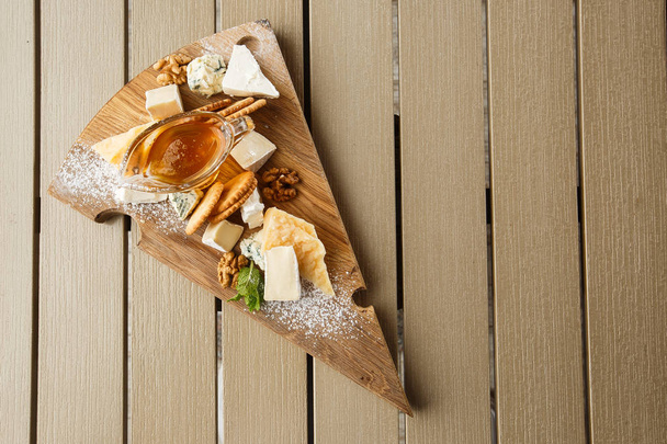 Tasting cheese dish on a wooden plate. Food for wine and romantic, cheese delicatessen on a wooden rustic table. Top view with copy space. - Photo, image
