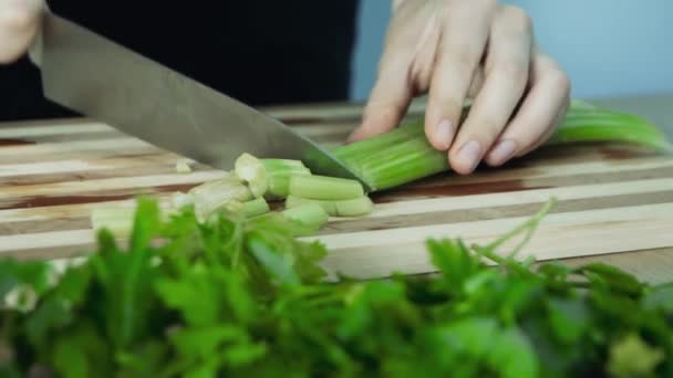 Knife chopping celery in kitchen on wooden cutting surface. Chef cutting celery to cook in the kitchen. Hands Slicing celery with Knife on chopping wooden board background.  - Footage, Video