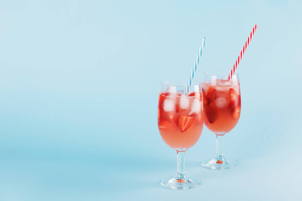 Свежий клубничный летний коктейль и кубики льда. Два бокала с клубникой, льдом и вином - клубничная сангрия на пастельно-голубом фоне, минимализм
 - Фото, изображение