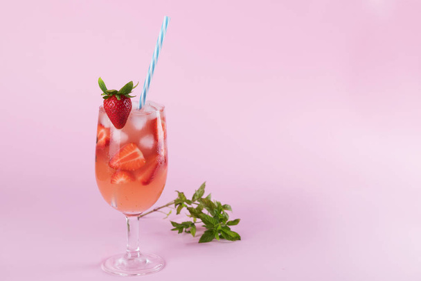 Sommercocktail mit frischen Erdbeeren und Eiswürfeln. Glas mit Erdbeere, Eis und Wein - Erdbeersangria auf pastellrosa Hintergrund, Minimalismus - Foto, Bild