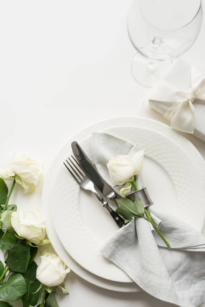 Romantic and wedding table setting with white rose, gift, dishware, silverware on white table. View from above. - Photo, Image