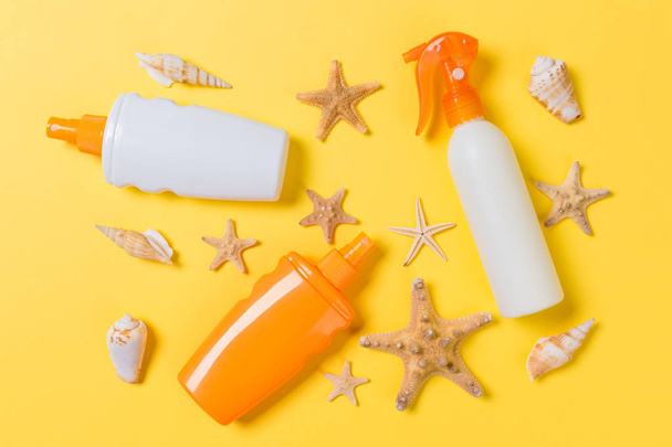 Sunscreen bottles with seashells on yellow table top view - 写真・画像