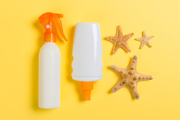 sarı arka plan üzerinde şişelerde denizyıldızı ve deniz kabukları ile güneş kremi, üst görünümü - Fotoğraf, Görsel