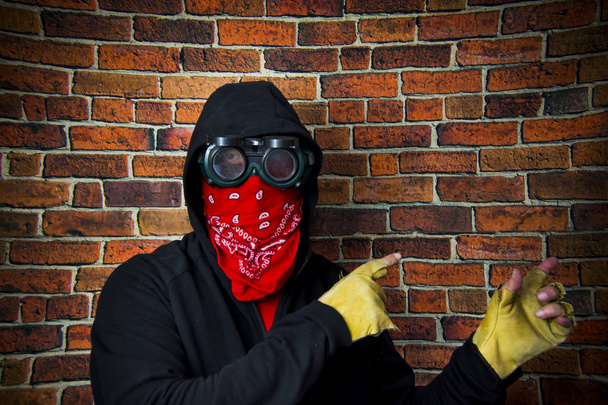 Homem escondido com capuz e lenço na frente de uma parede de tijolo
 - Foto, Imagem