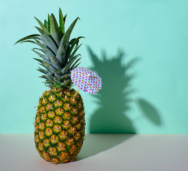 A pineapple with an umbrella with a clean pastel green background - Fotografie, Obrázek
