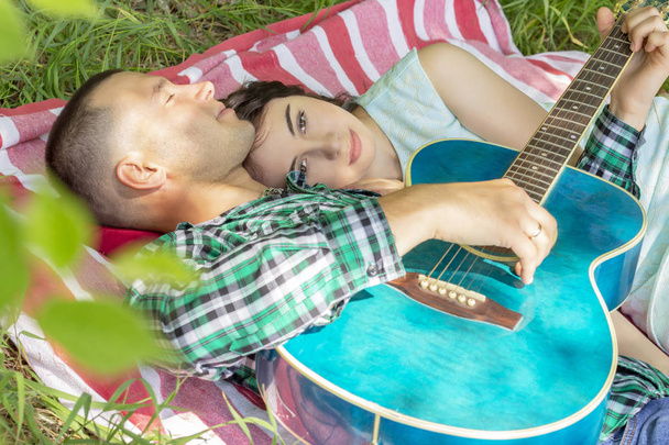 the guy plays the guitar to his girlfriend. romantic meeting. summer picnic couple laying on the grass - Fotó, kép