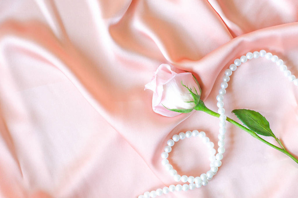 Rosa suavemente rosa con un collar de perlas en tela de satén
. - Foto, Imagen