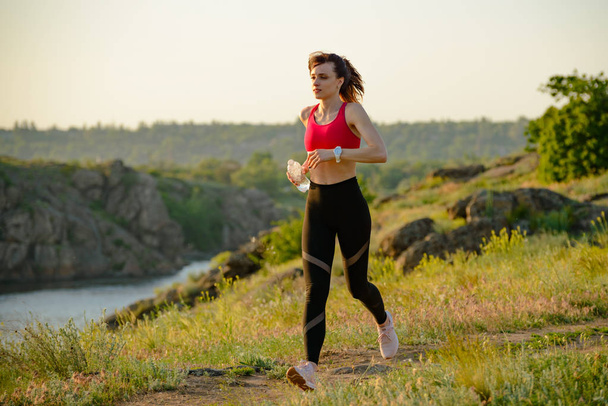 Young Beautiful Woman Running on the Mountain Trail in the Hot Summer Evening. Sport and Active Lifestyle Concept. - Photo, Image
