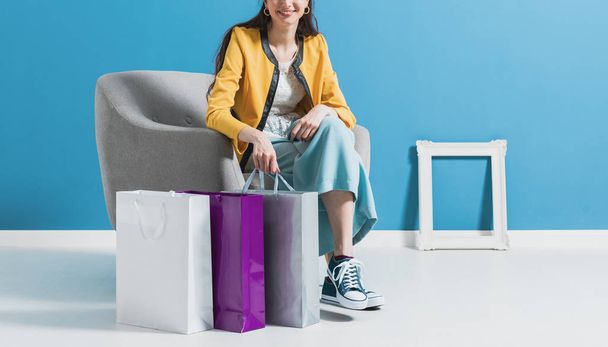 Glückliche Frau sitzt nach dem Einkaufen auf einem Sessel - Foto, Bild