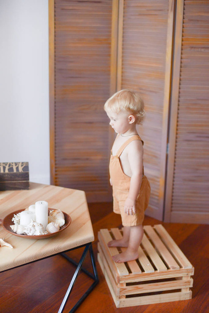 Μικρό χαριτωμένο μωρό με ξανθά σγουρά μαλλιά σε ένα ξύλινο τραπέζι με κοχύλια και κεριά. Οικολογική ζωή. Φυσικά υλικά. Υγιεινός τρόπος ζωής - Φωτογραφία, εικόνα