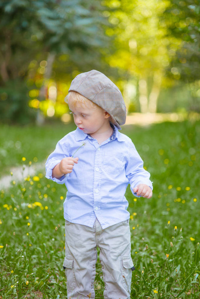 Mały chłopiec z blond włosami w WPR i niebieska koszula latem w polu z kwiatami - Zdjęcie, obraz