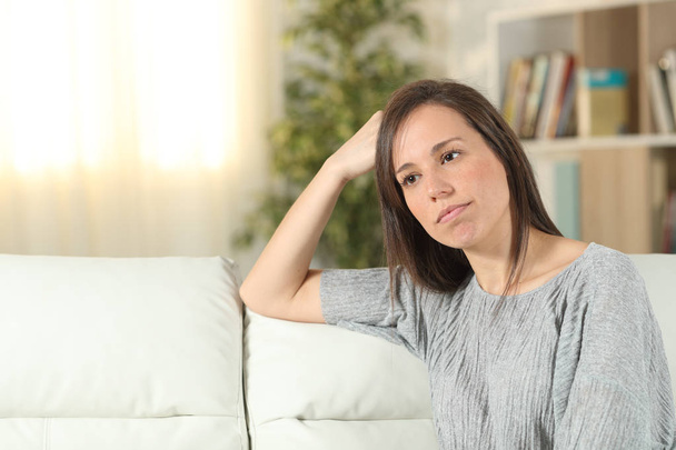 Pensive woman looking away on a couch at home - Foto, Bild