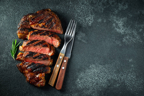 Sliced steak ribeye, grilled with pepper, garlic, salt and thyme on a dark stone background. Top view. Flat lay - Foto, Imagem