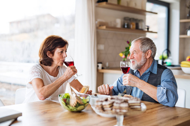 Senior couple with wine having lunch indoors at home, talking. - Foto, immagini