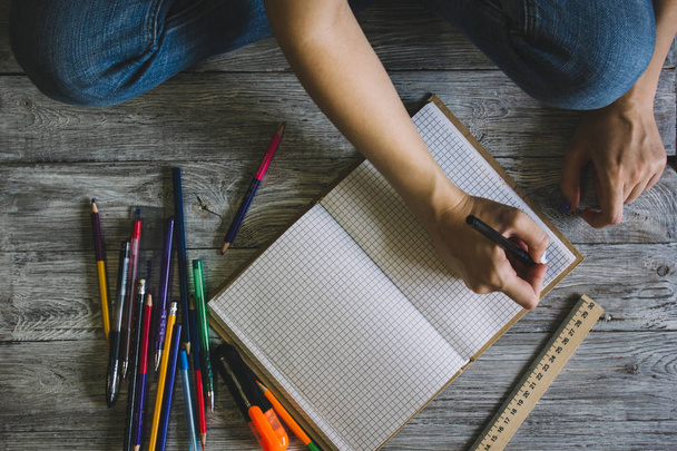 Rechtshänderin hält Stift beim Schreiben auf kleinem Notizbuch auf rostigem Holzboden - Foto, Bild