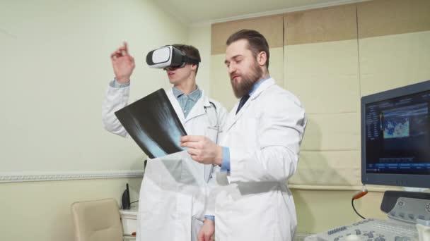 Врач использует 3D vr очки, в то время как его коллега осматривает рентген пациента
 - Кадры, видео