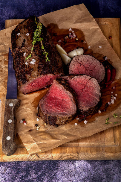 Bonfileden biftek Büyük bir parça parçalara ayrılır. Etin büyük bir kısmı tahta bir tahtada servis edilir. Yakın ve dikey yönlendirme.  - Fotoğraf, Görsel