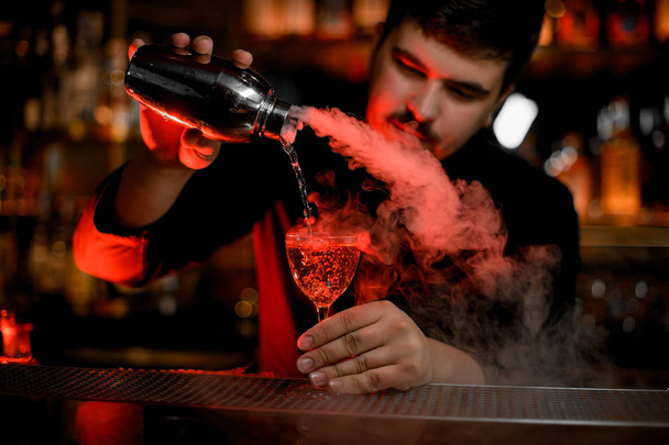 Male bartender with mustaches pouring a smoke into the cocktail glass from the shaker - Φωτογραφία, εικόνα