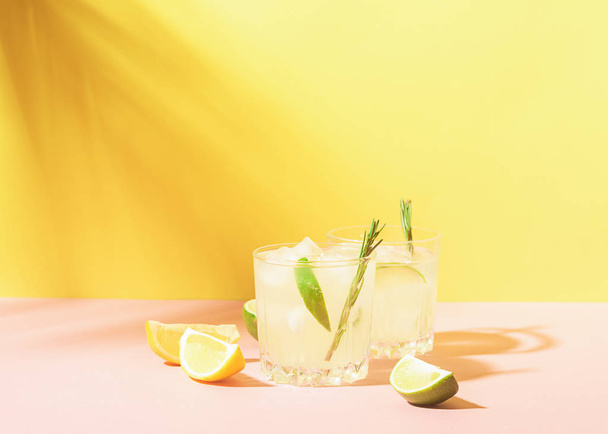 Getränk aus Zitrone und Limonade in durchsichtigen Gläsern auf pastellfarbenem Hintergrund mit hellem Sonnenlicht. Sommercocktail - Foto, Bild